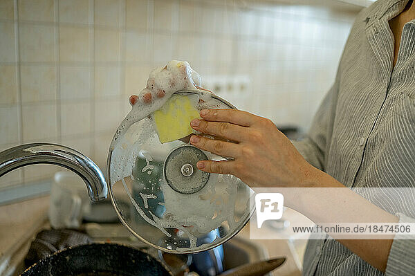 Frau wäscht Deckel mit Scheuerschwamm in der heimischen Küche