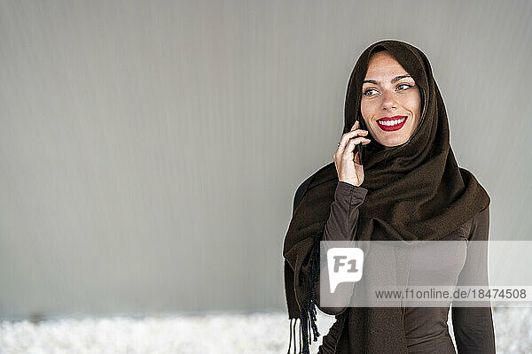 Frau trägt Hijab und spricht mit Smartphone vor der Wand