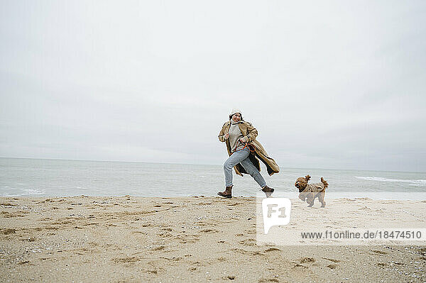 Frau läuft mit Hund im Sand am Strand