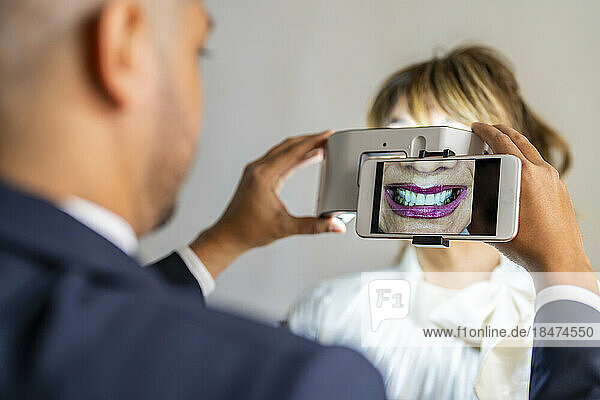 Businessman photographing colleague's smile through mobile phone using magnification equipment