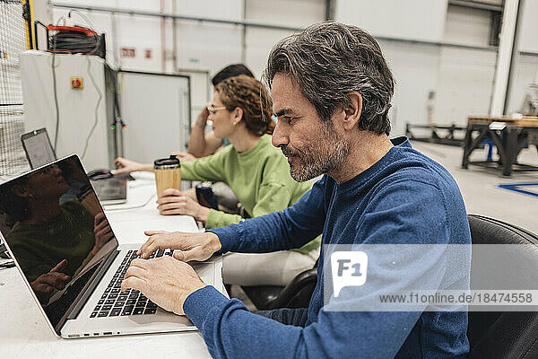 Engineer working on laptop sitting with colleagues in factory