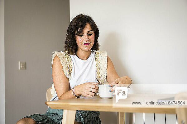 Lächelnde Frau  die zu Hause Kaffee auf dem Tisch trinkt