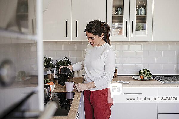 Woman pouring coffee in cup at kitchen