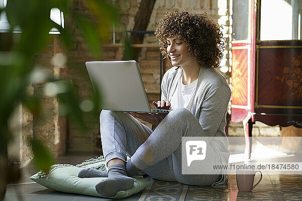 Happy freelancer using laptop sitting on floor at home
