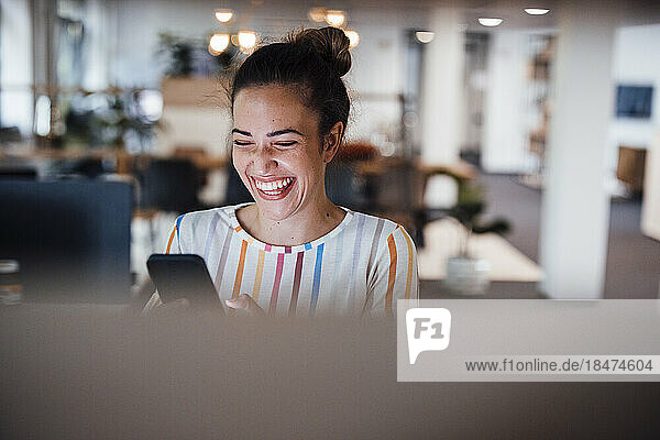 Cheerful businesswoman using mobile phone in office