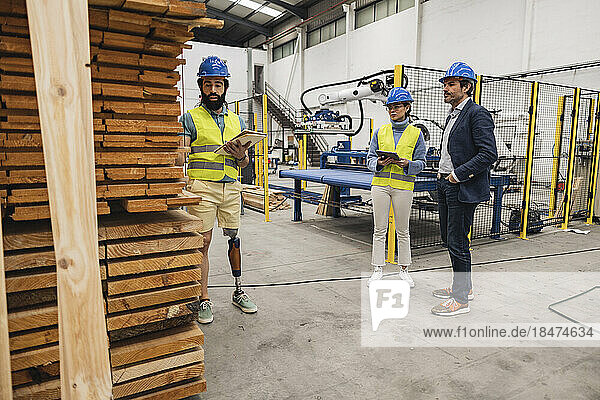 Engineer explaining by stack of planks with colleagues in factory