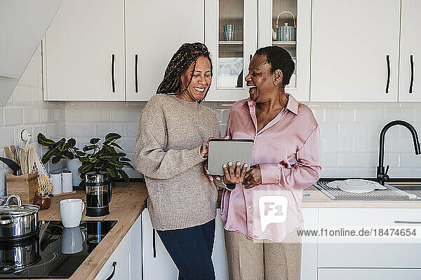 Woman sharing tablet PC with mother in kitchen at home