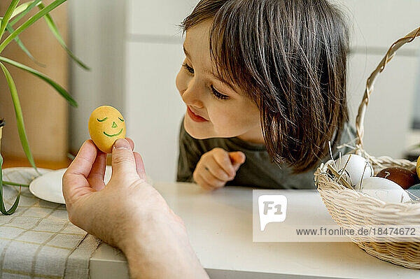 Lächelnder Junge blickt zu Hause auf dekoriertes Osterei