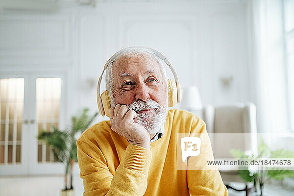 Thoughtful senior man listening to music through headphones at home