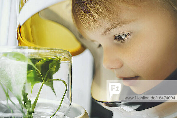 Girl wearing space helmet looking at small plant growing in glass jar