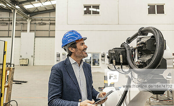 Happy engineer wearing hardhat looking at machine part in factory