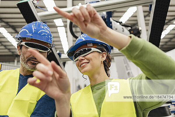 Engineer with colleague wearing smart glasses in robotics factory