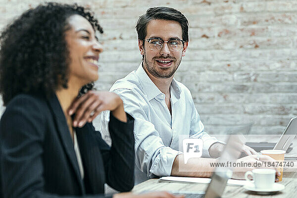 Happy businesswoman with colleague sitting at desk in office