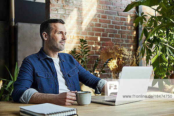 Thoughtful businessman with coffee cup at desk in loft office