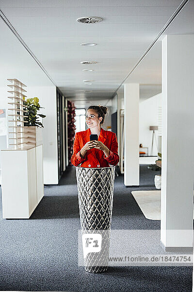 Happy young businesswoman using smart phone standing inside planter