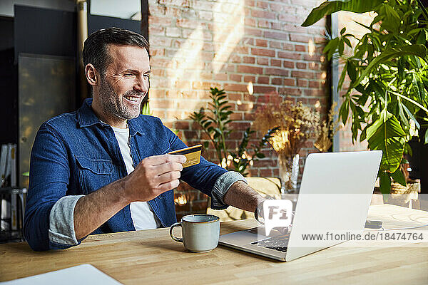 Happy businessman doing online shopping through credit card and laptop at loft office