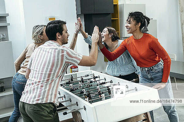 Cheerful colleagues playing foosball and giving high-five at office