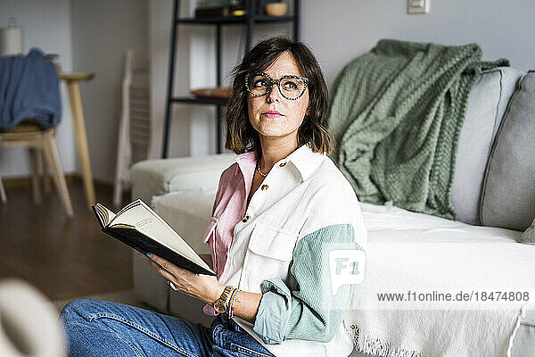 Nachdenkliche Frau sitzt mit Buch zu Hause