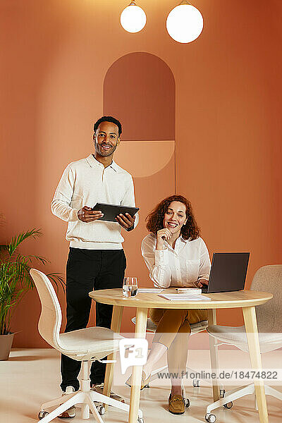 Young businessman holding tablet PC with colleague sitting at desk in office