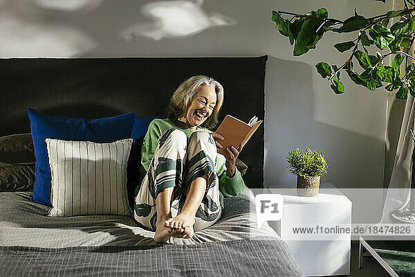Happy mature woman reading book on bed in bedroom