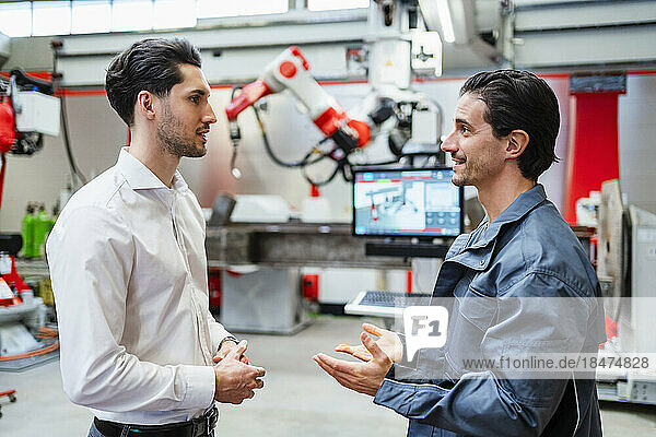 Smiling engineer talking to technician at robot factory
