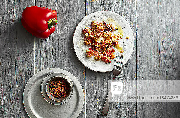 Raw bell pepper  chili powder and plate of ready-to-eat couscous