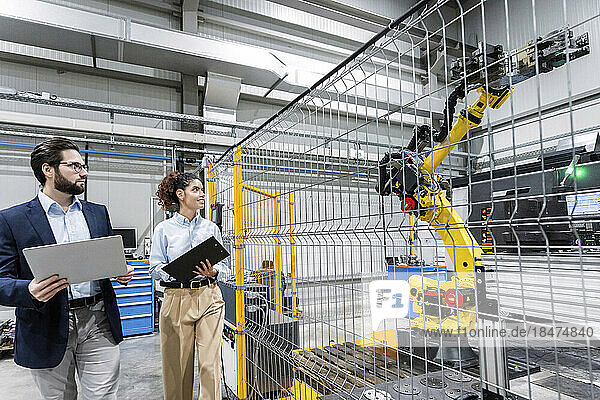 Business colleagues examining robotic arm in factory