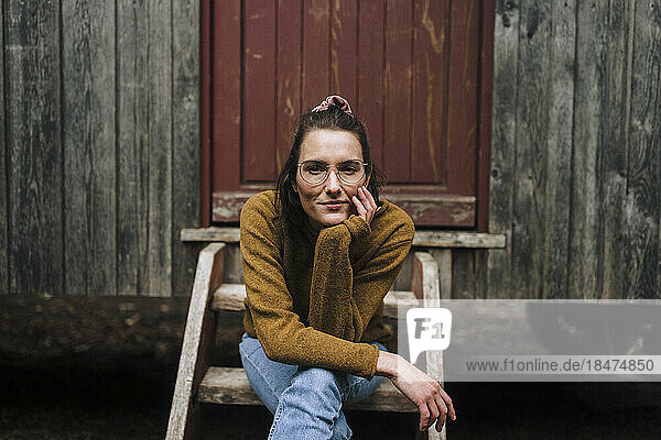 Smiling woman with hand on chin sitting in front of tiny house