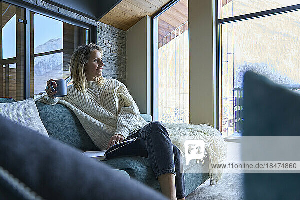 Thoughtful woman sitting with coffee on sofa at home