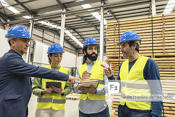 Mature engineer explaining colleagues over note pad in factory