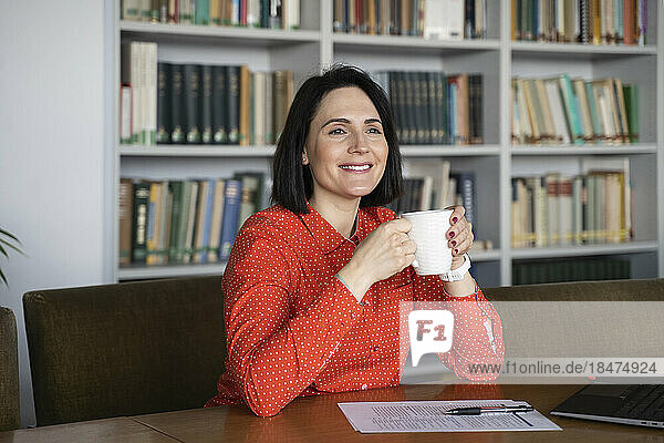 Happy businesswoman with coffee cup sitting at desk