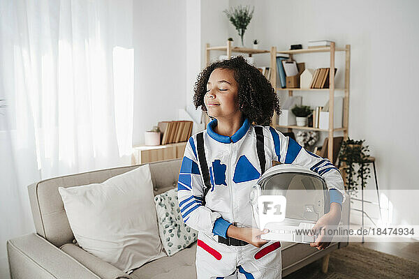 Smiling girl wearing space suit standing with eyes closed at home