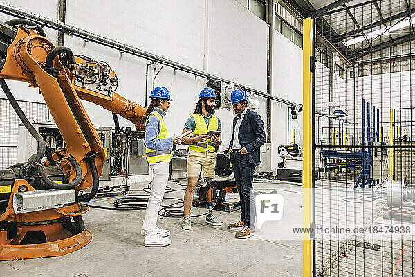 Engineer with colleagues wearing hardhat having discussions in factory