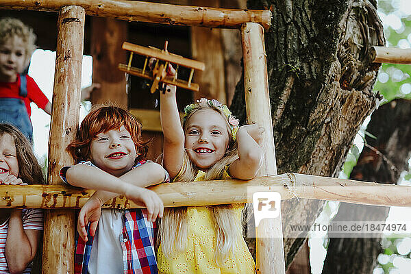 Smiling girl playing with toy airplane by friends on tree house