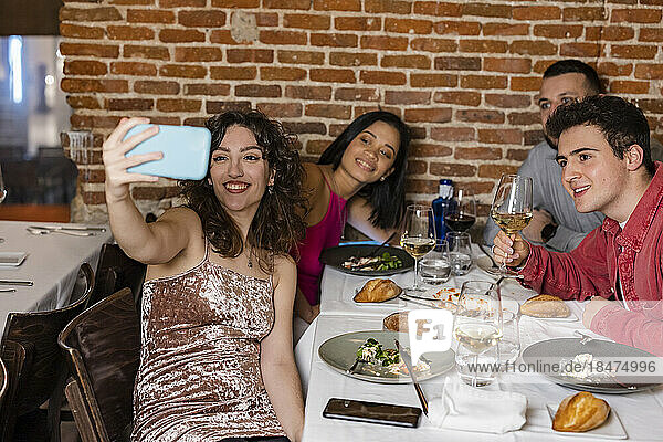 Happy woman taking selfie with friends at restaurant