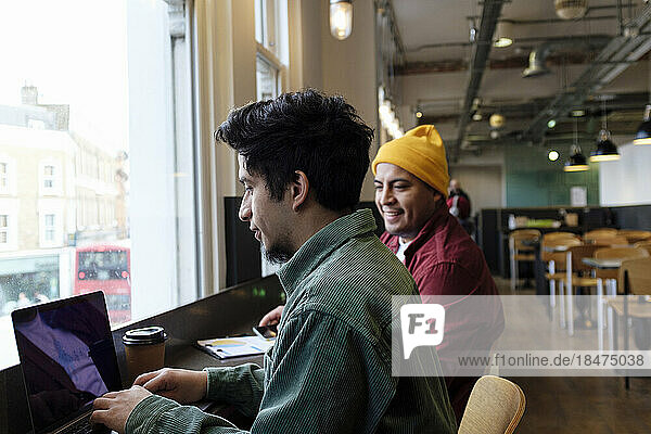 Young freelancer working on laptop with brother in cafe