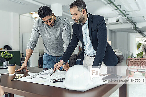 Businessman explaining and having discussion with colleague over blueprint at office
