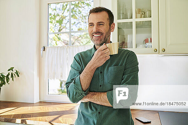 Mature man standing in kitchen drinking coffee