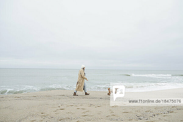 Frau spaziert mit Hund in Ufernähe am Strand