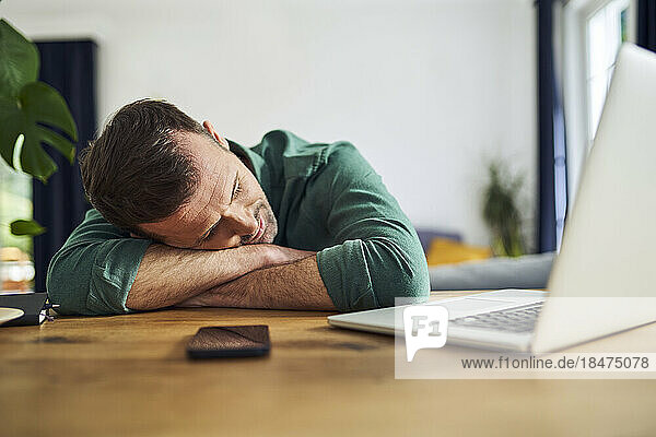 Overworked man sleeping on arms at desk