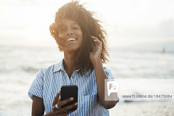 Happy woman with smart phone in front of sea at sunset