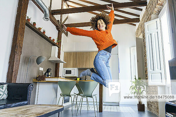 Happy woman with curly hair jumping at home