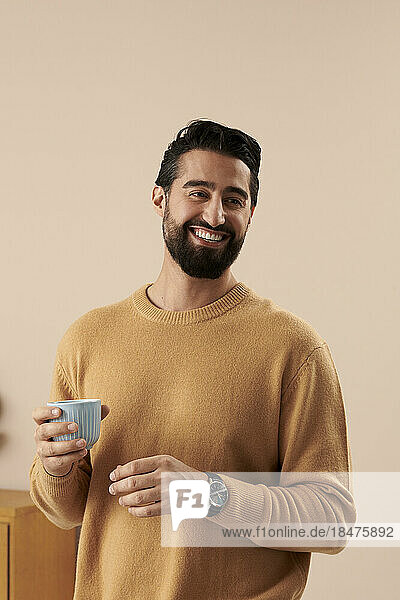 Happy man holding coffee cup in front of wall