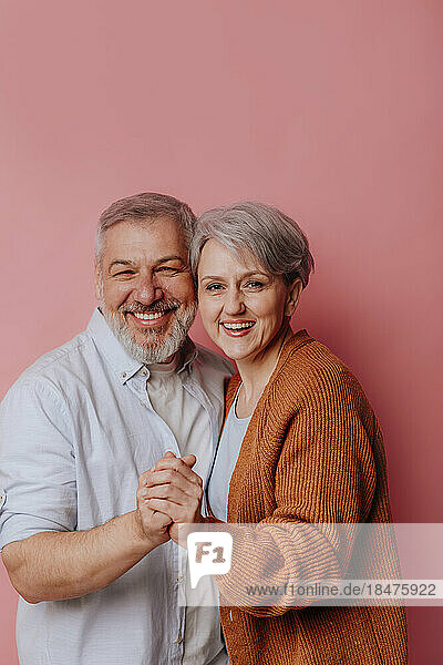 Happy mature couple standing against pink background