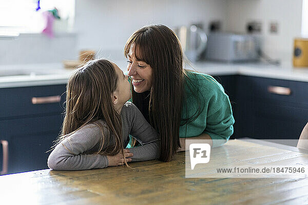 Glückliche Mutter umarmt ihre Tochter  die zu Hause am Tisch sitzt
