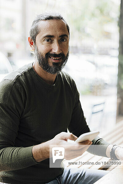 Smiling man using smart phone at table in cafe