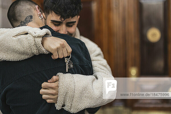 Gay couple with house key hugging each other in front of door