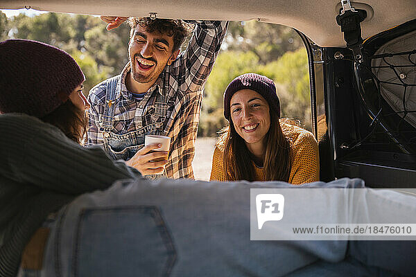Happy friends taking to woman in trunk of campervan