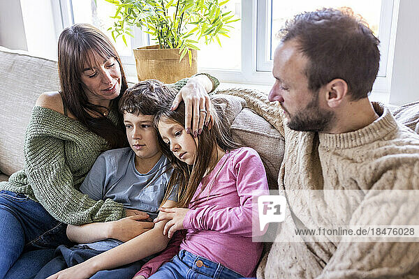 Happy woman embracing children with man sitting on sofa at home