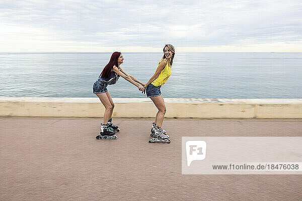 Friends roller skating and having fun at promenade by sea